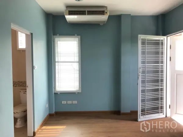 独立式住宅 出售在Bang Khen, Bangkok - 室内蓝色墙面，木地板，空调，百叶窗，带套卫的房间入口。