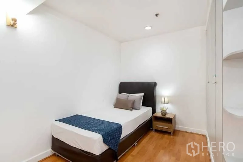 公寓 出租在Khlong Toei, Bangkok - 温馨单人卧室，床头灯、白色衣柜与暖色木地板。