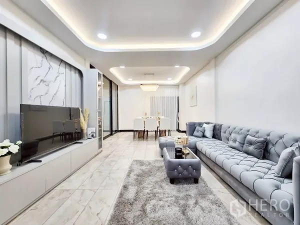 ทาวน์เฮาส์ ให้เช่าในHuai Khwang, Bangkok - ห้องนั่งเล่นสว่าง โซฟากำมะหยี่สีเทา พื้นลายหินอ่อน และผนังทีวีบิวท์อิน