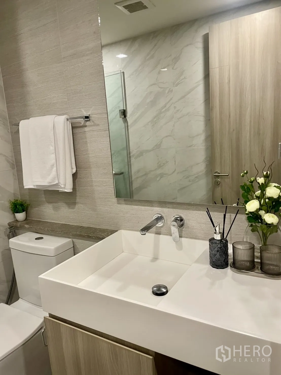 คอนโด ให้เช่าในWatthana, Bangkok - เคาน์เตอร์อ่างล้างหน้าในห้องน้ำ พร้อมแจกันดอกไม้ กระจกบานใหญ่ และกระเบื้องลายหินอ่อน
