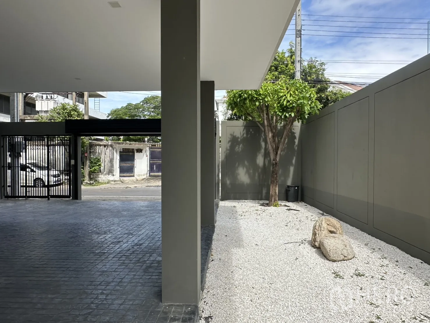 Home Office for rent or sale in Suan Luang, Bangkok - Covered driveway with black gate beside a gravel garden with tree and boulders.