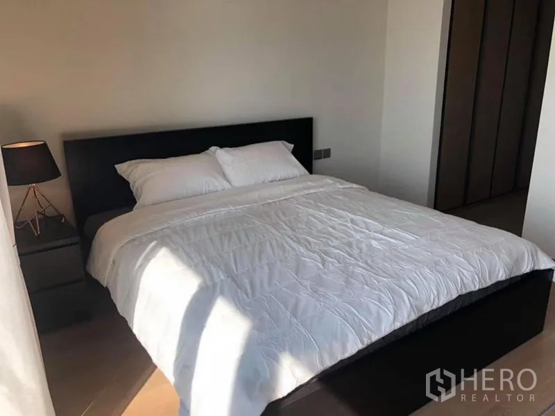 Condominium for rent in Khlong Toei, Bangkok - Bright bedroom with double bed, bedside lamp, and built-in wardrobe.