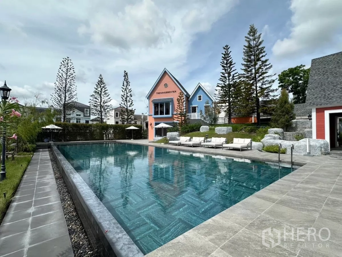 联排别墅 出租在Prawet, Bangkok - 户外泳池，躺椅和粉彩色会所建筑。