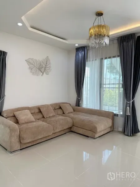 Townhouse for rent in Bang Phli, Samut Prakan - Bright living room featuring an L-shaped sofa, large windows with sheer curtains and a chandelier.