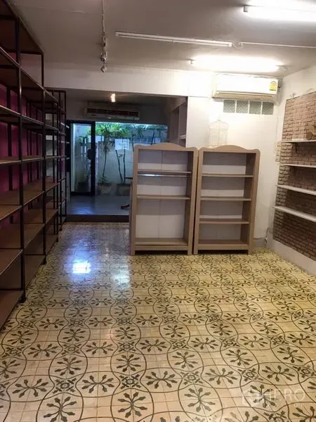 零售空间 出租在Khlong Toei, Bangkok - 店铺室内配复古花纹地砖、金属层架、展示柜与空调，后部为通向小天井的玻璃门。