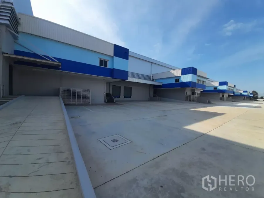 Factory for rent in Bang Lamung, Chon Buri - Exterior loading docks with ramps, blue-and-white cladding and a wide concrete yard.