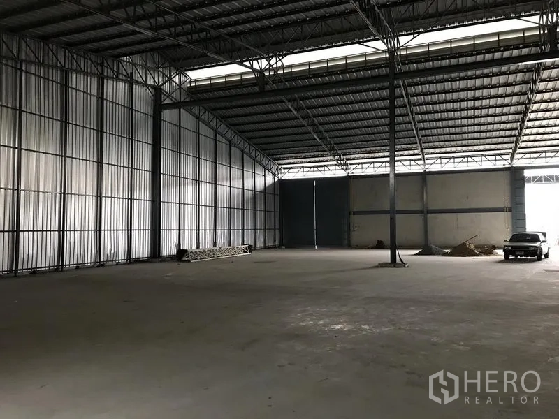 Warehouse for rent in Bang Phli, Samut Prakan - Spacious warehouse interior with high steel truss roof, concrete floor, and large sliding doors.