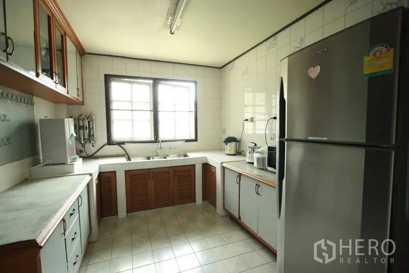 Detached House for rent in Bang Phli, Samut Prakan - Practical kitchen with tiled walls, ample countertops, wooden cabinets and a stainless refrigerator.