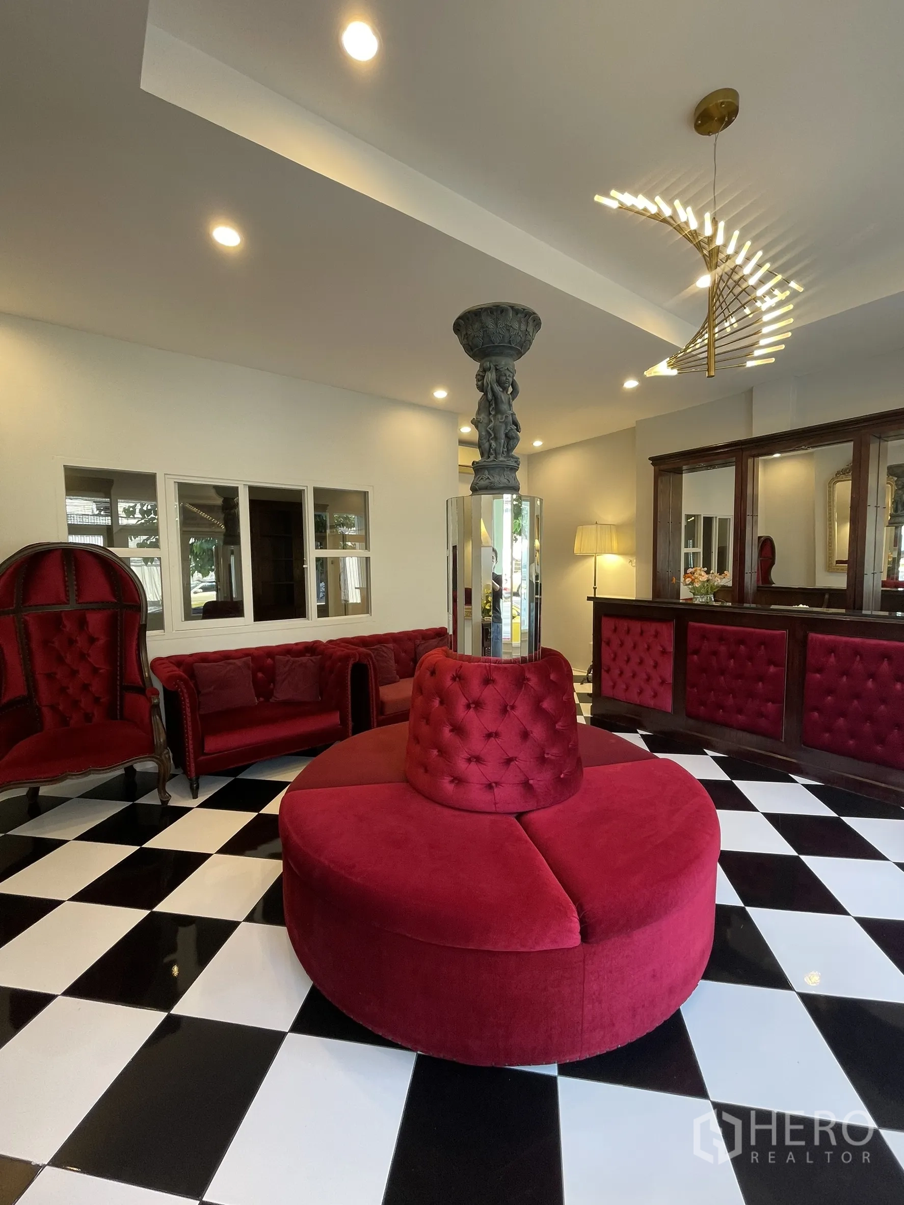 Shophouse for rent in Bang Kapi, Bangkok - Elegant lobby with black‑and‑white checkerboard floor, red velvet seating, sculptural column and modern chandelier.