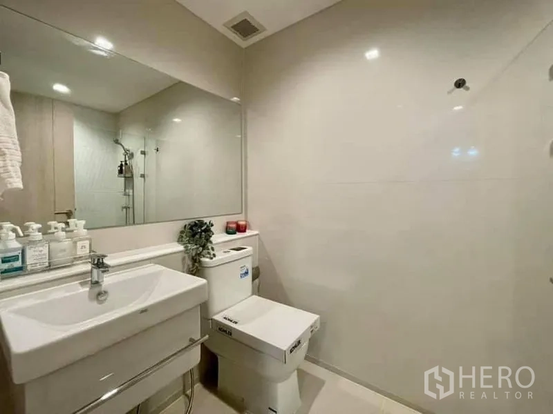 Condominium for rent in Pathum Wan, Bangkok - Bright bathroom with wall-mounted sink, large mirror and Kohler toilet in neutral tones.
