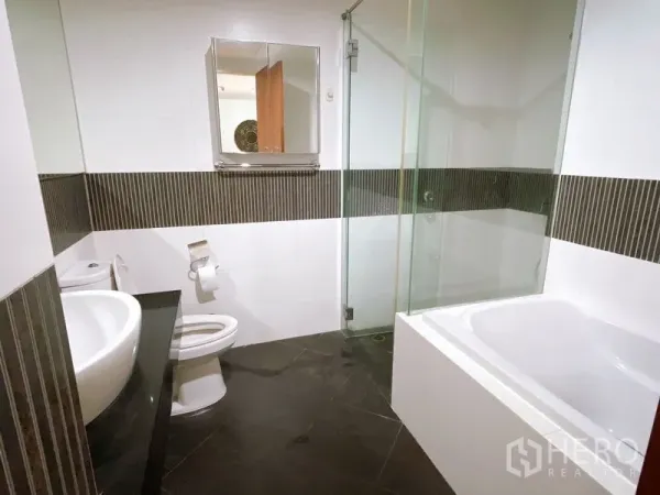 Condominium for rent or sale in Sathon, Bangkok - Modern bathroom with bathtub, glass shower screen, vanity sink and striped tile accents.