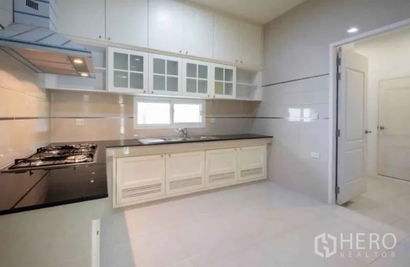 Detached House for rent or sale in Bang Phli, Samut Prakan - Bright Thai kitchen with white cabinetry, black granite countertop, gas hob and a window.