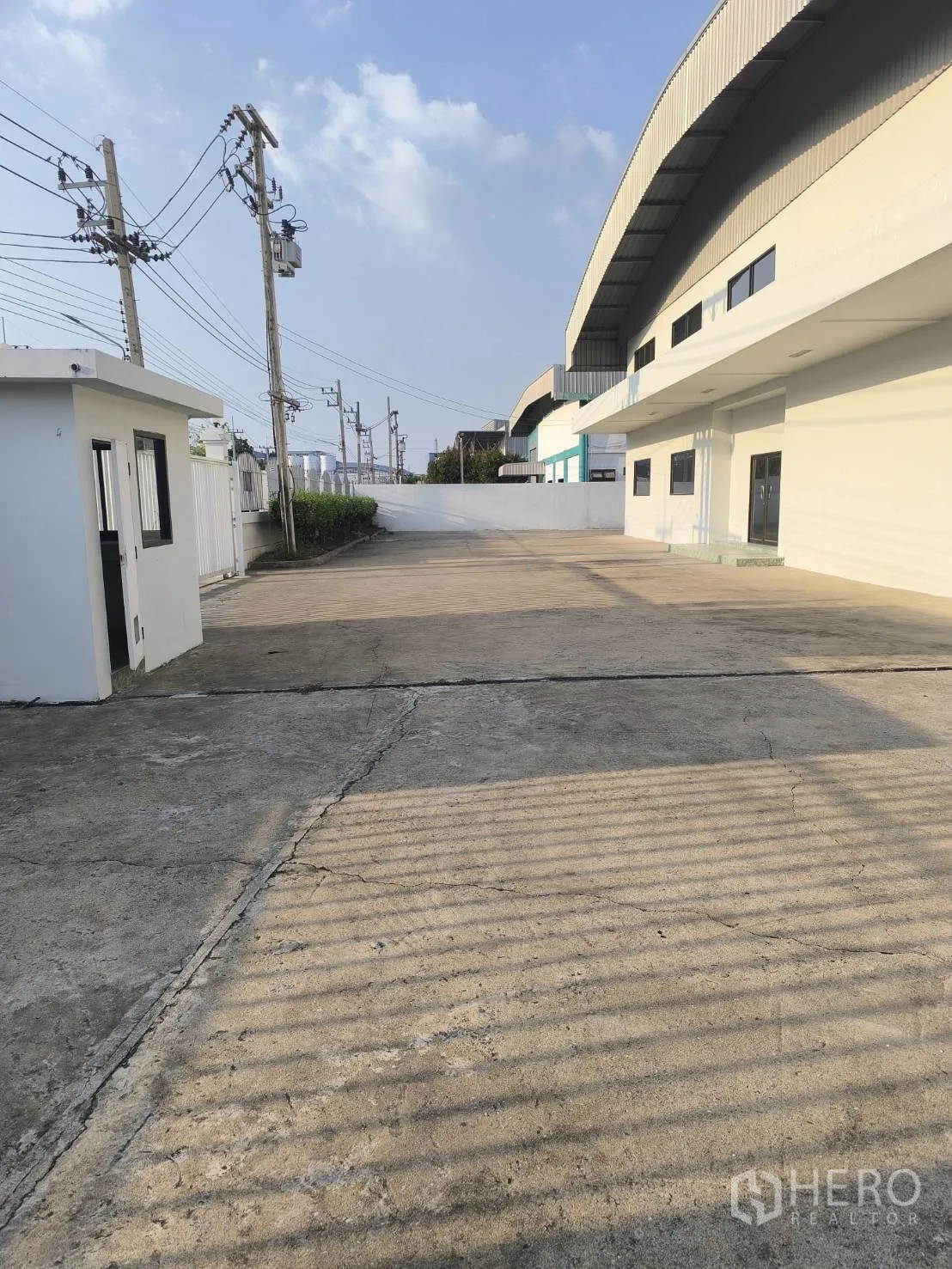 Factory for sale in Khlong Luang, Pathum Thani - Wide concrete driveway beside the building with a small guardhouse.