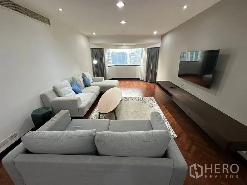 คอนโด ให้เช่าในWatthana, Bangkok - ห้องนั่งเล่นสว่าง โซฟาสีเทา ทีวีติดผนัง และหน้าต่างเว้าเห็นวิวเมือง