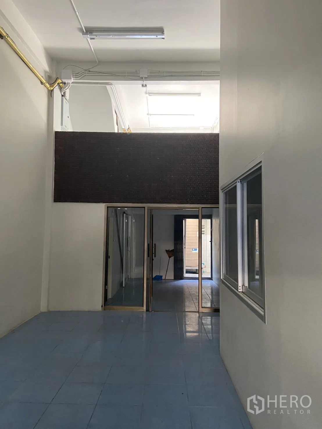 店屋 出租在Bang Na, Bangkok - 一层挑高大厅，蓝色地砖与玻璃推拉隔断通向后方