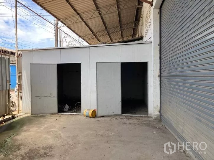 Factory for rent in Bang Phli, Samut Prakan - Exterior loading area with three service rooms and a large roll-up shutter beneath a canopy.