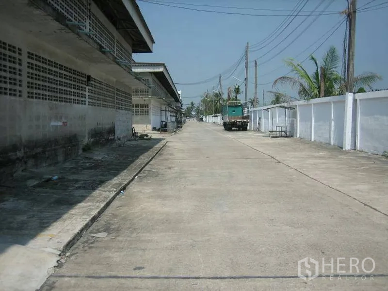Warehouse for rent in Min Buri, Bangkok - Wide concrete access road beside warehouse blocks with power lines and truck-friendly driveway inside a secure compound in Min Buri.