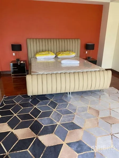 บ้าน ให้เช่าในSuan Luang, Bangkok - ห้องนอนใหญ่เตียงบุนวม ผนังสีส้ม และพรมลายเรขาคณิตบนพื้นไม้