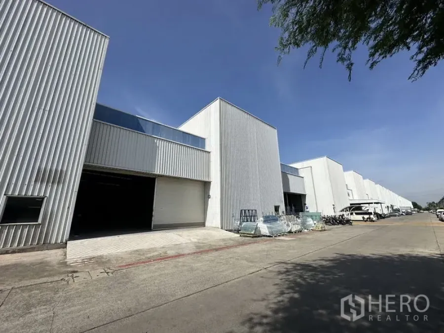 工厂 出租在Khlong Luang, Pathum Thani - 空銮县一排现代白色厂房，宽阔车道与装卸口，蓝天下的外观。