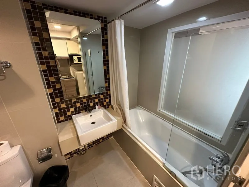 Apartment for rent in Khlong Toei, Bangkok - Bathroom with bathtub, glass screen, mosaic-tile mirror and vanity.