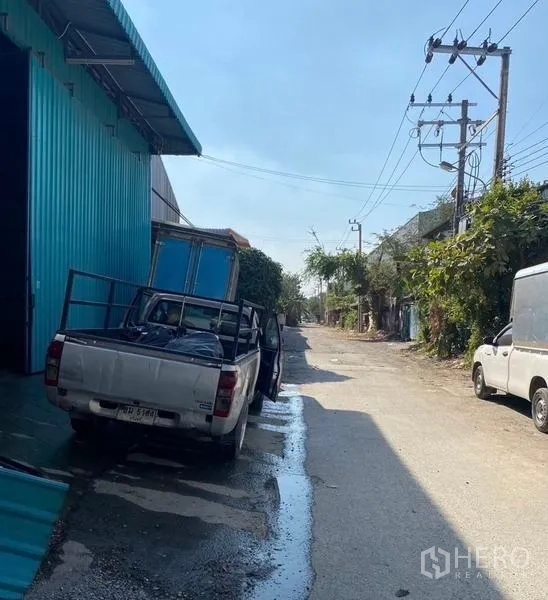 คลังสินค้า ให้เช่าในBang Kapi, Bangkok - ด้านข้างโกดังสีน้ำเงินติดถนนกว้าง มีเสาไฟและรถกระบะจอด เข้าออกสะดวก