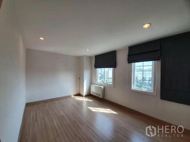 联排别墅 出租在Bang Na, Bangkok - 转角大卧室，双面窗、遮光罗马帘、嵌灯与木地板。