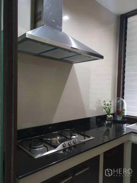 Detached House for sale in Watthana, Bangkok - Compact kitchen with black granite counter, gas cooktop and stainless steel hood.