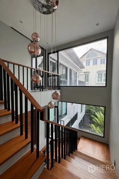 Semi-detached House for rent in Watthana, Bangkok - Wooden staircase with black balustrade, large windows, and pendant lights.