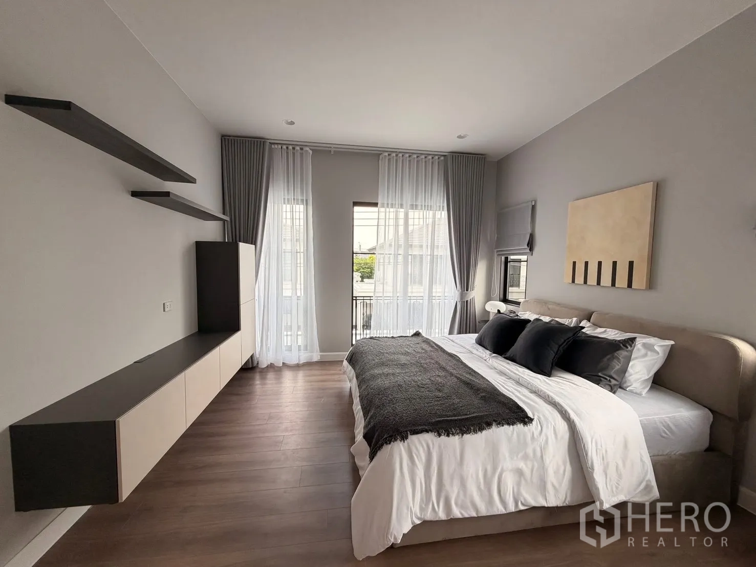 Detached House for rent in Bang Phli, Samut Prakan - Spacious bedroom with king bed, wood floors, balcony window, and floating shelves.