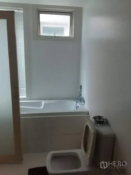 公寓 出租在Ratchathewi, Bangkok - 白色浴室，带浴缸与小窗，配磨砂推拉门。