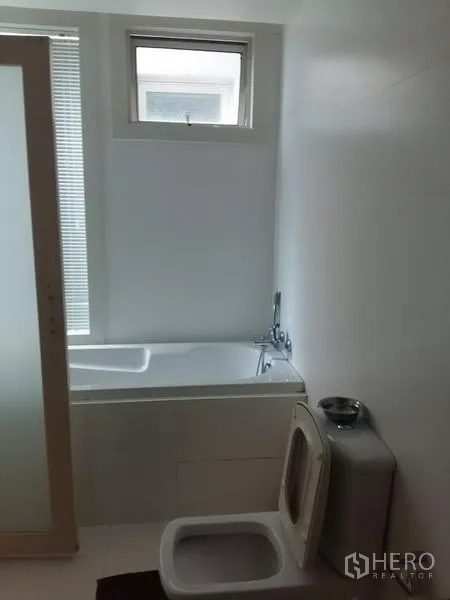 公寓 出租在Ratchathewi, Bangkok - 白色浴室，带浴缸与小窗，配磨砂推拉门。