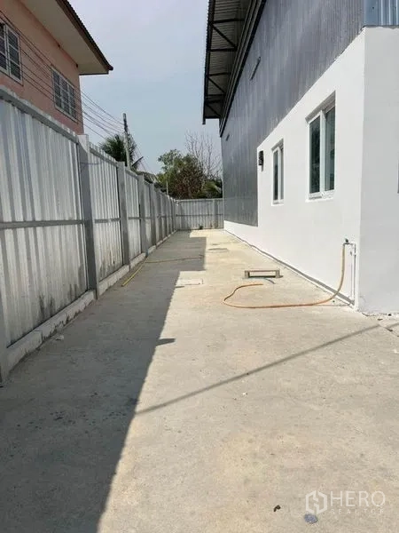 Warehouse for rent in Nonthaburi - Concrete side yard along the building with windows and utility lines for drainage and water.