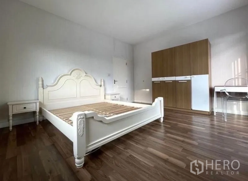 Detached House for rent in Prawet, Bangkok - Large secondary bedroom with classic white bed frame, wood floors, wardrobe and desk.