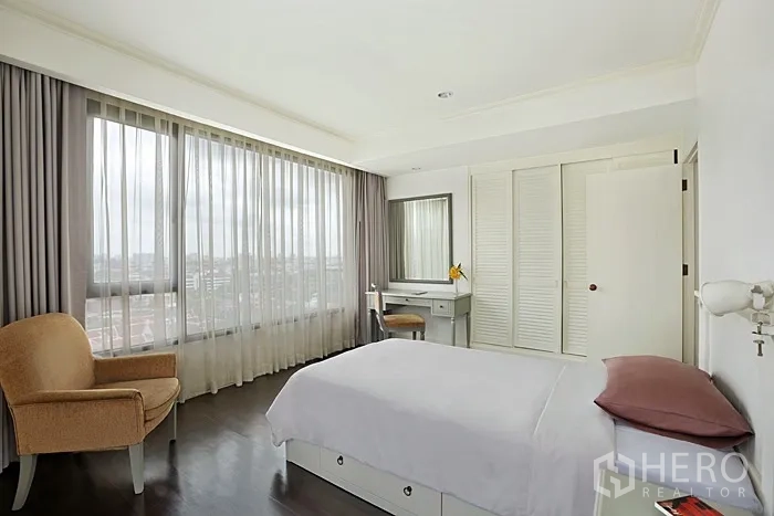 Condominium for rent in Khlong San, Bangkok - Bright bedroom with large windows, sheer curtains, armchair, built-in wardrobe and a vanity desk.