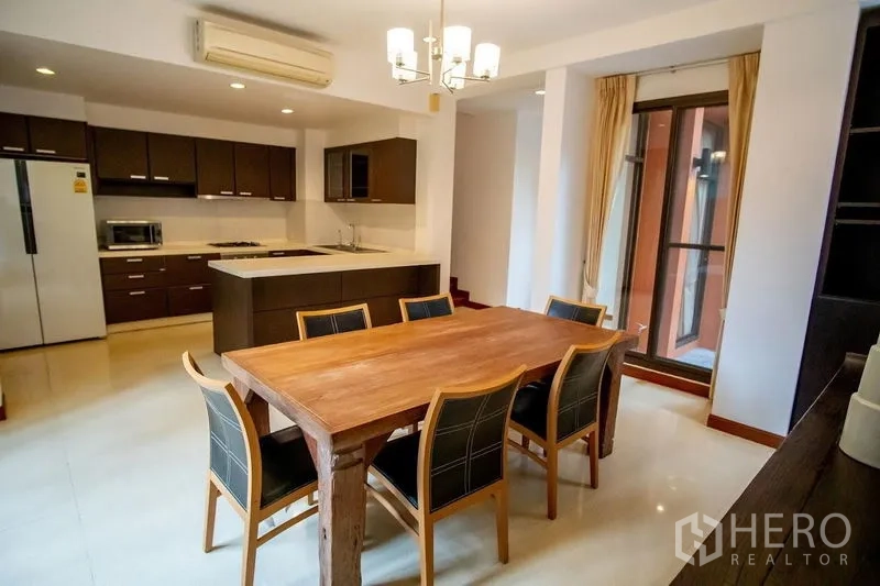 Townhouse for rent in Watthana, Bangkok - Open-plan kitchen and dining area with island, dark cabinets, and ample space.