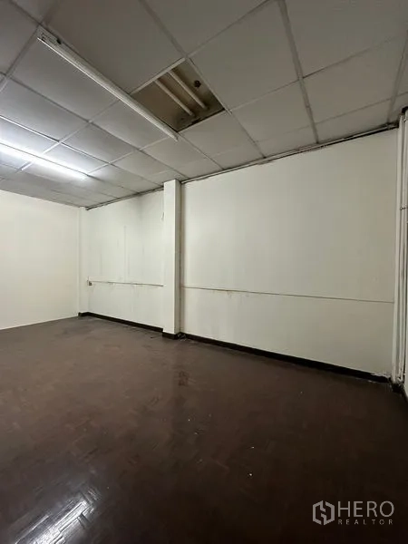 Shophouse for rent in Sathon, Bangkok - Empty room with drop ceiling, white walls, and dark wood flooring ready for customization.