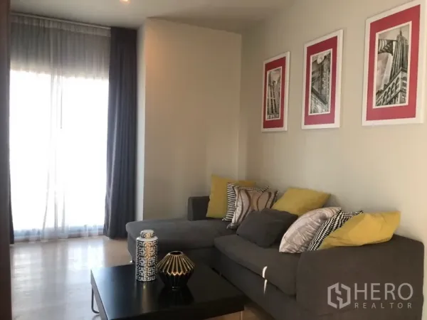 公寓 出租或出售在Bangkok - 明亮客厅，转角沙发、彩色抱枕与茶几，墙面挂画点缀。