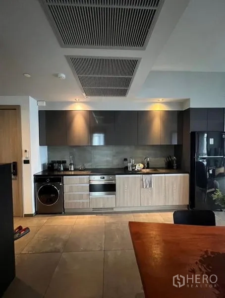Condominium for rent in Watthana, Bangkok - Sleek linear kitchen with built-in oven, cooktop, washer and dark cabinets.