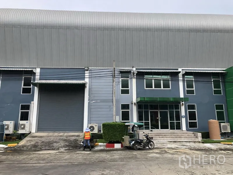 Factory for rent in Samut Prakan - Front elevation of the factory showing a large loading roller door and glass‑fronted office entry.