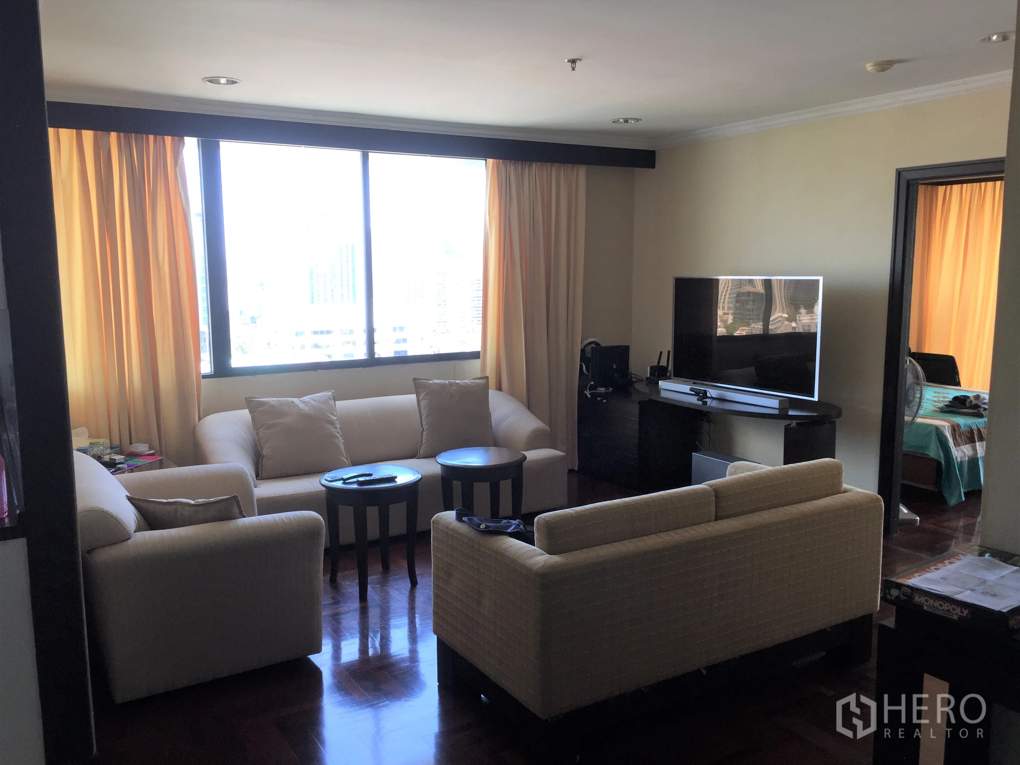 Condominium for rent or sale in Khlong Toei, Bangkok - Living room with cream sofas, TV console and big window offering skyline views.