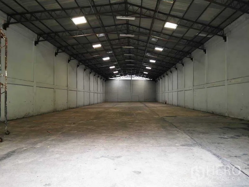 Warehouse for rent in Khlong Toei, Bangkok - Long clear-span storage hall with metal truss ceiling and evenly lit concrete flooring.