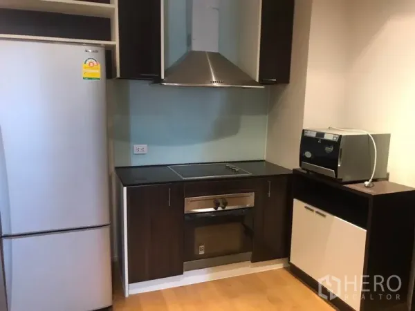 Condominium for rent in Watthana, Bangkok - Built-in kitchen featuring cooktop, oven, range hood, microwave, and a stainless refrigerator.