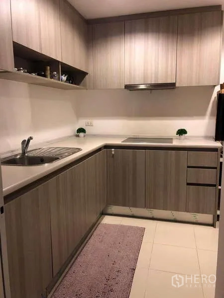Condominium for sale in Huai Khwang, Bangkok - U-shaped kitchen with upper and lower cabinets, sink and electric cooktop.