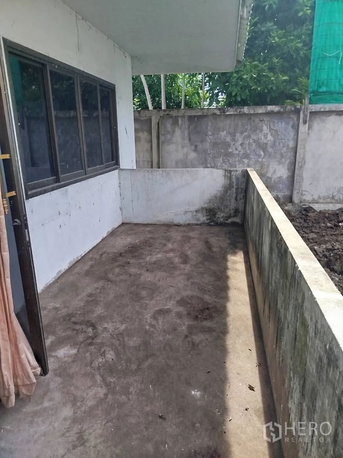 Detached House for rent or sale in Bang Na, Bangkok - Covered side patio with concrete floor and low wall overlooking the yard.