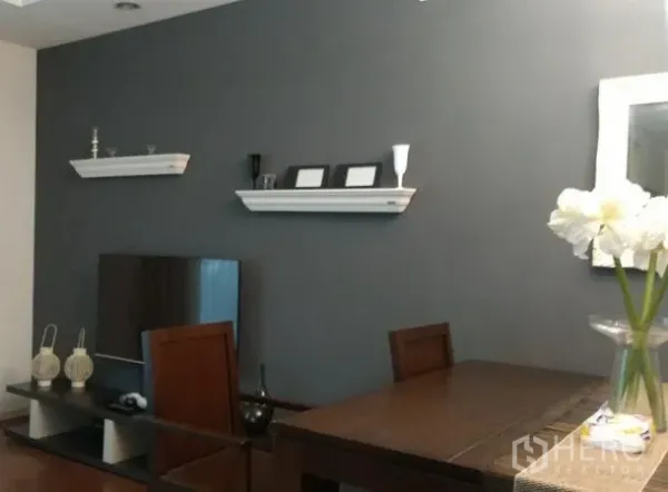 คอนโด ให้เช่าในKhlong Toei, Bangkok - มุมรับประทานอาหารพร้อมโต๊ะไม้ ข้างชั้นวางทีวี และผนังเทาแต่งชั้นลอย