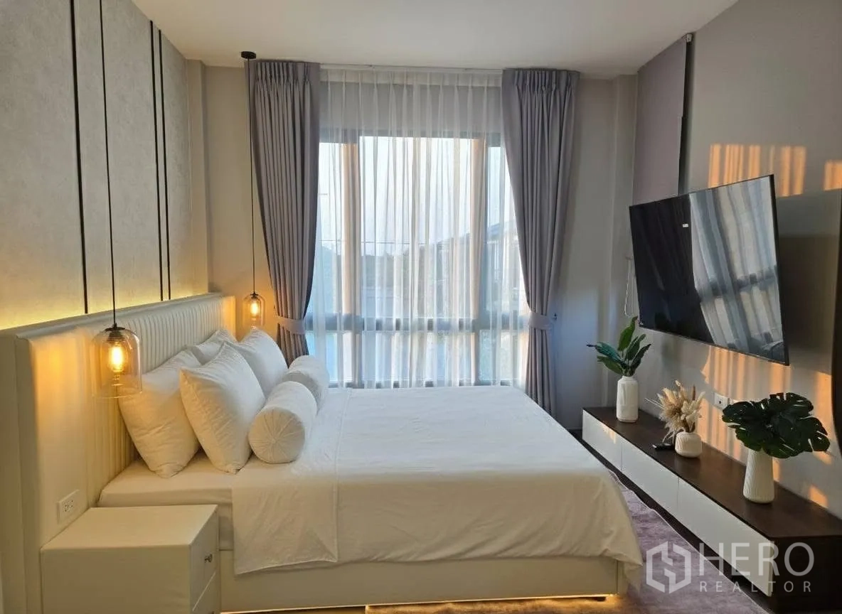 Detached House for rent or sale in Bang Phli, Samut Prakan - Master bedroom with pendant bedside lights, wall-mounted TV, and full-height curtained windows.
