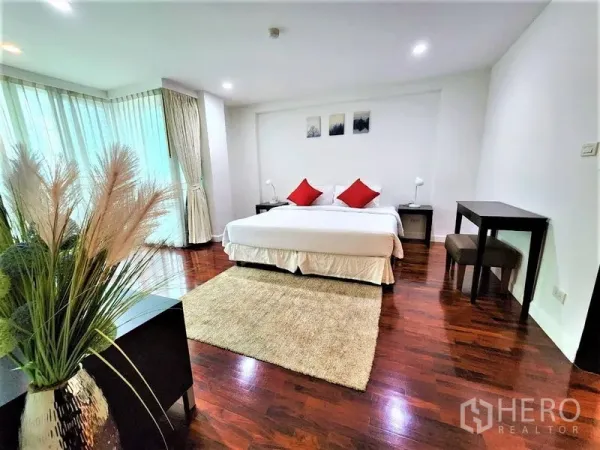 公寓 出租在Bang Rak, Bangkok - 宽敞主卧，特大床与红色靠枕，转角落地窗和光亮木地板。