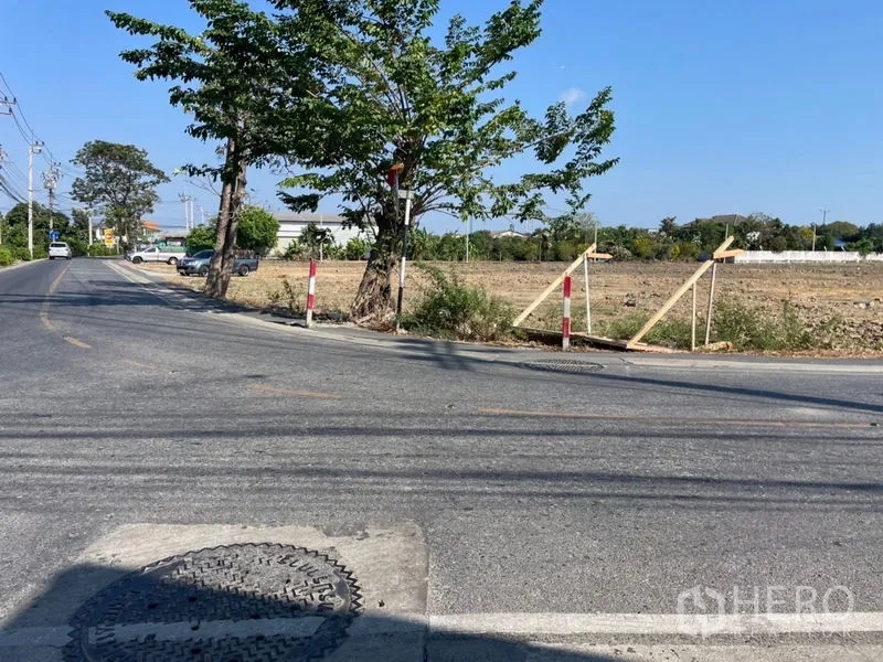 Land for sale in Mueang Samut Prakan, Samut Prakan - Roadside frontage of the plot with boundary markers and tree shade along a paved street
