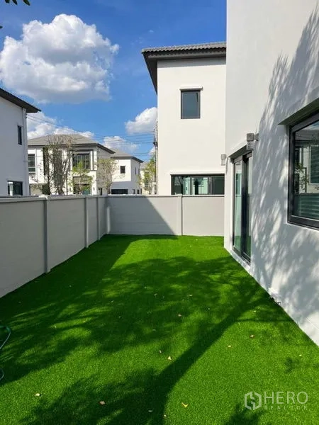 Detached House for rent or sale in Samut Prakan - Private side yard with high walls and green artificial lawn.