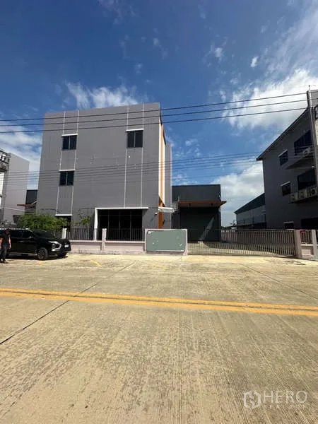 Factory for rent in Lam Luk Ka, Pathum Thani - Modern three-storey office and factory facade with gated driveway under blue sky in an industrial area.